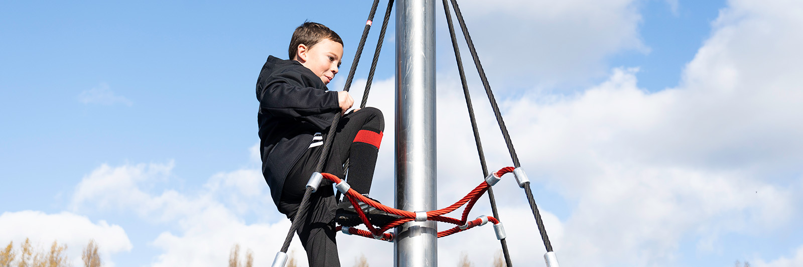 A young boy has made it to the top of a climbing net cone.